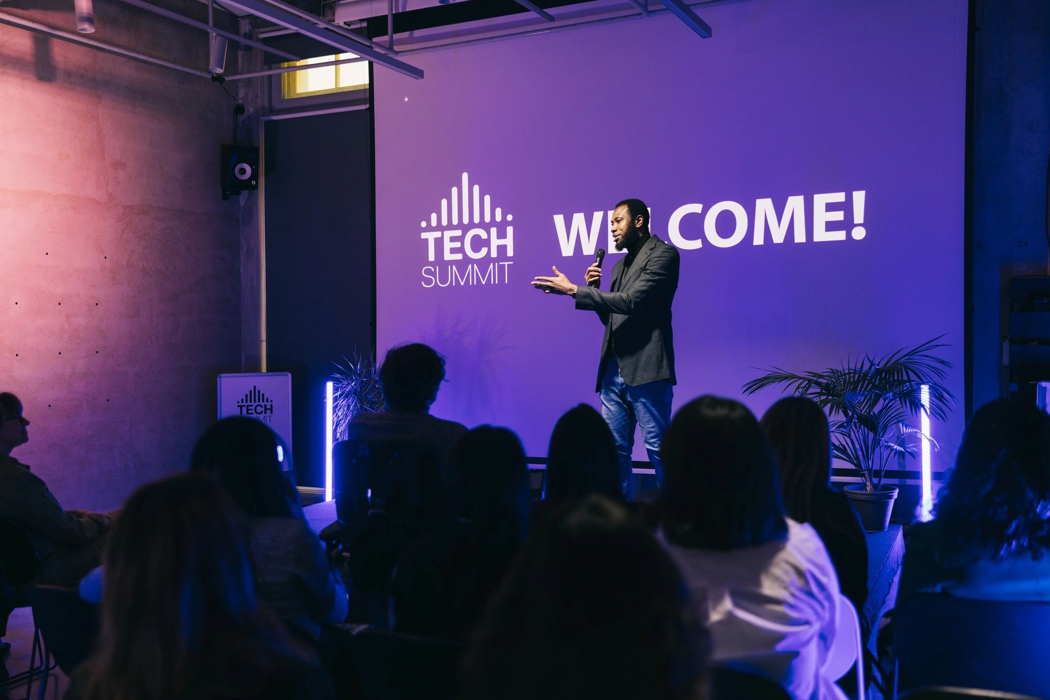 Presenter on stage at a tech conference with large screen